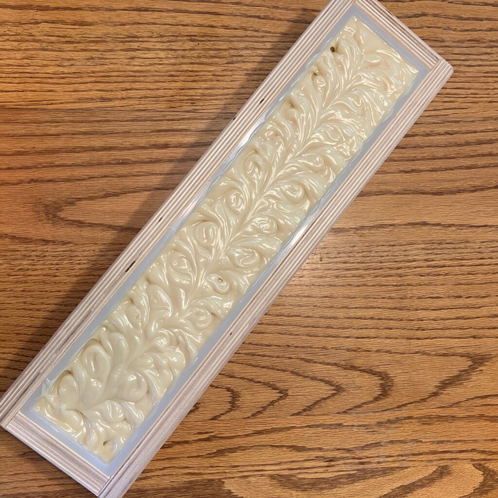 Cream-colored soap with a textured top in a long, thin wooden mold.
