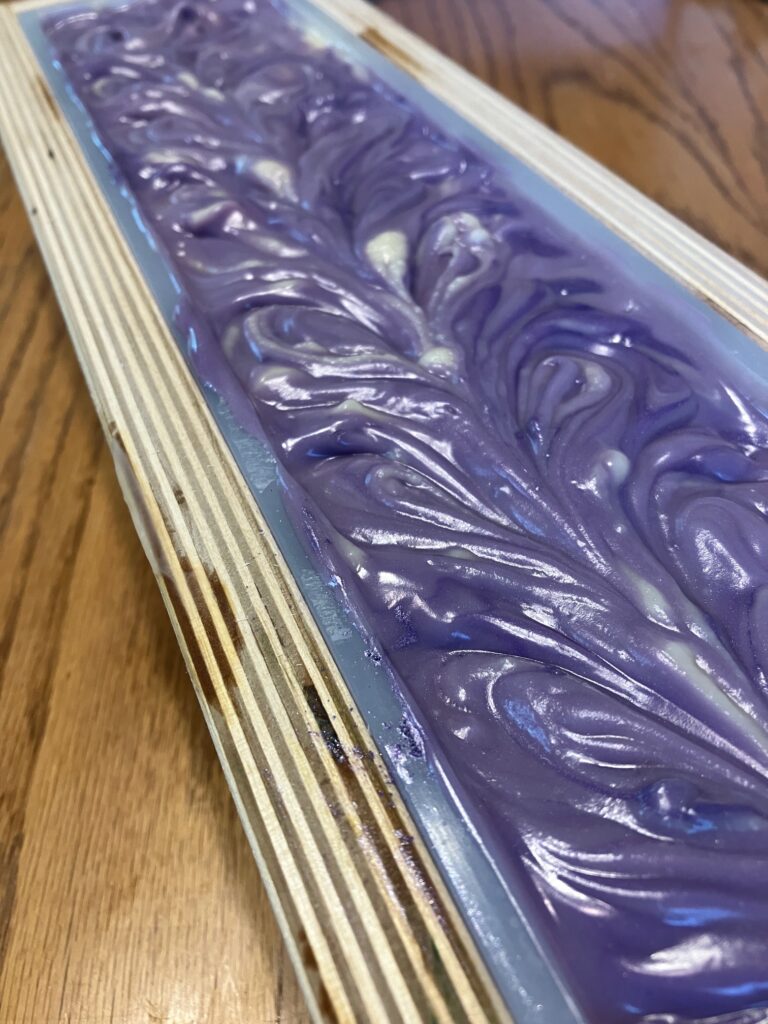 Purple soap with a textured, swirled top in a wooden mold.