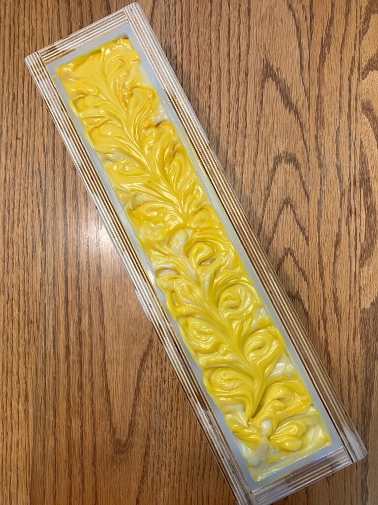 Yellow and white soap with a textured, swirled top in a wooden mold.